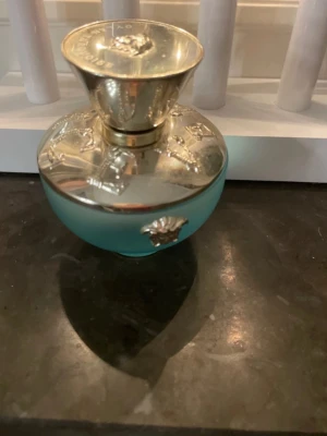 Versace Dylan Turquoise parfym - Versace Dylan Turquoise är en parfym i en snygg blå flaska med exklusiva gulddetaljer. Perfekt för dig som vill ha en lyxig touch i din doftsamling. Märkets ikoniska Medusa-symbol syns tydligt på locket. Helt full, aldrig använt!