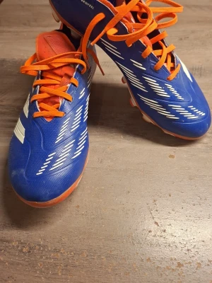 Adidas Predator blå fotbollsskor - Säljer ett par Adidas Predator fotbollsskor På grund av att dom var för små för mig. Skorna har snörning, låg profil och mönstrad ovandel i syntetmaterial. Sulan har dobbar i vitt och orange för bra grepp på planen. Perfekta för dig som vill sticka ut på matchen!