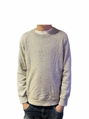 Grå sweatshirt från 157, storlek 150 - Enkel och stilren grå sweatshirt från 157 i storlek 150. Tröjan har rund halsringning, ribbade muddar vid ärmslut och nederkant samt lång ärm. Perfekt till jeans eller över en t-shirt för en chill look.