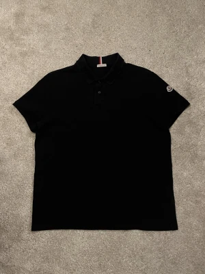Moncler Piké Navy tricolor - Hej! Säljer denna stilrena Moncler piké i färgen Navy! Modellen heter ”Maglia Polo Manica Corta” och det speciella med just denna pikén är att den har den snygga detaljen vid kragen! Pikén är helt felfri och är hel o ren! Storleken är Egentligen XL men är liten i storlek och rekommenderar att köpa denna om du vanligtvis bär Medium! Jag kan lösa en bild som passform vid begäran 🤝denna är autentisk! (Se industries lapp samt logga). Mvh