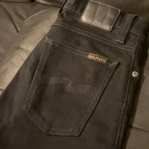 Svarta skinny jeans från Nudie Jeans - Svarta jeans från Nudie Jeans med klassisk femficksdesign och snygga detaljer på bakfickan. Modellen är skinny med smal passform och midwaist. Materialet är mjukt och stretchigt jeans, perfekt för dig som gillar en tajt look. Jag köpte dom för 1500kr nya och säljer dom för dom för 699. Priset är inte hugget i sten vid snabb affär 