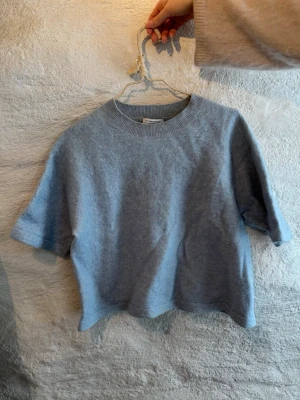 Ljusblå stickad topp med kort ärm - Mysig ljusblå stickad topp med korta ärmar och rund halsringning. Toppen har en enkel, clean look och är lite croppad i modellen. 