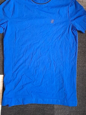 Blå t-shirt från Lyle & Scott - En stilren blå t-shirt från Lyle & Scott med liten broderad logga på bröstet. Klassisk rund halsringning och korta ärmar. Perfekt till jeans eller shorts för en enkel och snygg look.