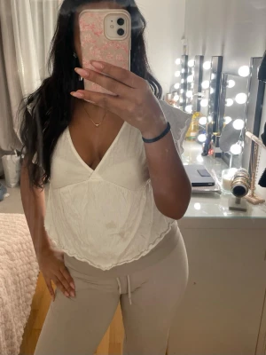 Vit blus med volangärmar - Säljer en söt vit blus med v-ringning och volangdetaljer på ärmarna. Toppen har en luftig passform och är tillverkad i ett lätt bomullstyg, perfekt för varmare dagar. Den har en feminin och avslappnad stil som passar till många olika outfits.