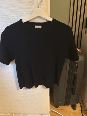 Svart stickad t-shirt  - En stilren svart stickad t-shirt från hm. Modellen  har en enkel, klassisk design som passar till jeans. Perfekt för dig som gillar en clean och tidlös look.