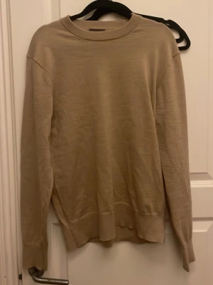 Beige långärmad tröja i bomull - En enkel och stilren beige tröja från H&M i storlek S med rund halsringning och långa ärmar. Tillverkad i mjuk bomull och har ribbade muddar vid ärmslut och nederkant. Perfekt för lager på lager under höst och vår.