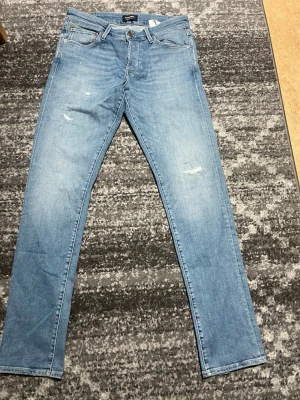 Ljusblå jeans från Jack & Jones slim glenn - Säljer ett par ljusblå jeans från Jack & Jones med klassisk femficksdesign och diskreta slitningar framtill. Jeansen har rak passform och normal midja. Tillverkade i mjukt bomullsmaterial för en bekväm känsla. Perfekta till sneakers och hoodie.