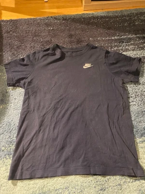 Nike tröja  - Nike t-shirt – Storlek XS 🖤 Snygg och stilren Nike t-shirt i mörk färg med liten logga på bröstet ✨ Perfekt för både vardag och träning 💪 ✔️ Storlek: XS ✔️ Skick: Använd men i bra skick ✔️ Passform: Klassisk och bekväm ✔️ Original Nike Lätt att matcha med jeans, mjukisbyxor eller shorts 👟 Skicka gärna meddelande vid frågor eller fler bilder 📩😊