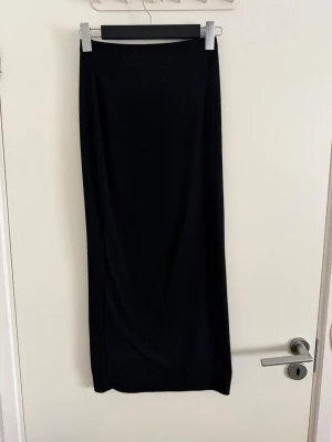 Svart långkjol i mjukt material - Enkel och stilren svart långkjol med rak passform. Kjolen är i ett mjukt, stretchigt material som sitter snyggt på kroppen. Perfekt att matcha med en crop top eller stickad tröja. Inga synliga detaljer eller mönster. Använd fåtal gånger.