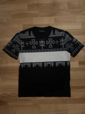 Svart och vit t-shirt från Givenchy - Snygg svart t-shirt från Givenchy med vit panel över bröstet och coolt grafiskt mönster i grått och vitt. T-shirten har korta ärmar och rund halsringning. Materialet är mjuk bomull som känns skönt mot huden. Perfekt för dig som vill sticka ut med en unik designerpiece.