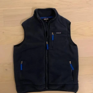 Mörkblå fleeceväst från Patagonia - Mysig mörkblå fleeceväst från Patagonia med hög krage och tre fickor med dragkedja och blå detaljer. HÖR AV DIG VID MINSTA FUNDERING!!!💸