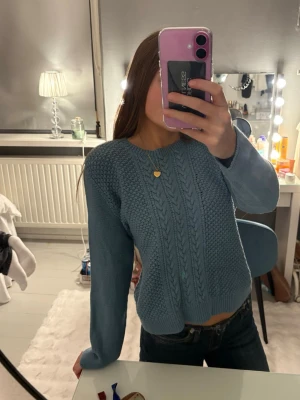 Blå stickad tröja med mönster - Mysig blå stickad tröja med kabelstickat mönster framtill och ribbade muddar. Tröjan har en klassisk rund halsringning och långa ärmar. Väldigt varm så perfekt för kalla dagar eller en sommarkväll❣️
