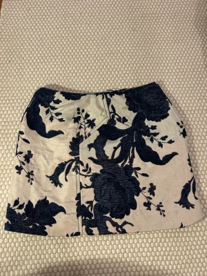 Blommig kortkjol från Baum und Pferdgarten - Supersnygg kortkjol med mörkblått blommönster på beige botten från Baum und Pferdgarten. Kjolen har en rak passform och är fodrad för extra komfort. Materialet känns rejält och har en exklusiv känsla. Perfekt att styla med boots eller sneakers.