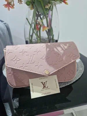  rosa axelväska i skinn - Supersnygg rosa axelväska. Väskan har guldfärgade detaljer, dragkedja och matchande plånbok. Perfekt storlek för det viktigaste och ger en lyxig touch till din outfit.