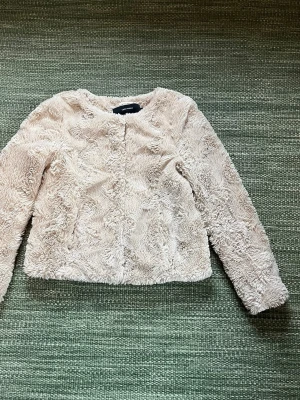Beige pälsjacka från Vero Moda - Säljer en fluffig och mjuk beige pälsjacka/kofta från Vero Moda i storlek XS. Jackan har rund halsringning, långa ärmar och stängs med tryckknappar framtill. Perfekt för dig som vill ha en cozy look med lite extra stil.
