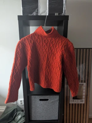 Stickad orange kabel stickad polotröja - Säljer en riktigt snygg orange stickad polotröja med flätmönster. Tröjan har hög krage.. Den är lite croppad och har en mysig, chunky känsla som gör den superbekväm. Passar xs