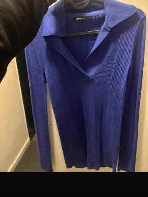 Kornblå ribbad tröja Gina Tricot - Snygg kornblå ribbad tröja från Gina Tricot med krage och v-ringning. Tröjan har långa ärmar och är figurnära i modellen, perfekt för att lyfta din outfit med en pop av färg. Materialet är stretchigt och mjukt för skön passform.