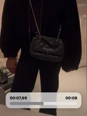 Svart quiltad handväska från Valentino - Snygg svart quiltad handväska från Valentino med guldfärgade detaljer och kedjerem. Väskan har ett elegant mönster och logga framtill. Perfekt accessoar för att lyfta din outfit.