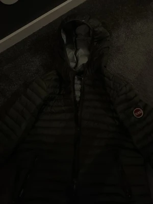 Svart dunjacka från Colmar med huva - Snygg svart dunjacka från Colmar med huva och dragkedja framtill. Jackan har quiltad design, två sidofickor med dragkedja och Colmar-logga på ärmen. Perfekt för kalla dagar och riktigt skön att bära.