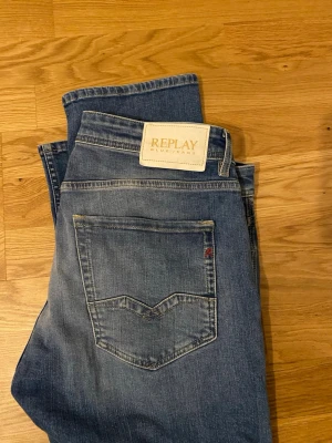 Blå Replay jeans straight fit - Snygga blå jeans från Replay med klassisk femficksdesign och raka ben. Jeansen har ljusa slitningar framtill och bakficka med diskret logga. Tillverkade i mjukt bomullstyg för en bekväm känsla. Perfekta för en avslappnad stil.