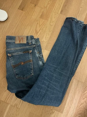 Blå jeans från Nudie Jeans - Säljer nu ett par riktigt fräscha blå jeans från Nudie i super skick och till ett fint pris. Det finns ett litet hål i en av fickorna, men påverkar inte jeansens funktion. Jeansen är storlek 31/32 och har normal passform och perfekt för en chill stil. Vid minsta fråga är det bara skicka ett meddelande!