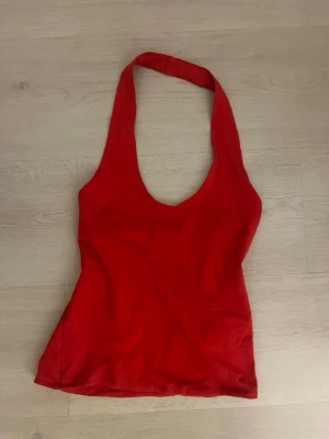 Röd halterneck linnetopp - Snygg röd halterneck topp i mjukt bomullstyg. Toppen är ärmlös och har en djup urringning framtill, perfekt för en trendig och avslappnad look. Passar till både jeans och kjol för en cool stil.