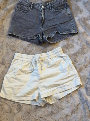 Två par shorts, denim och beiga linne shorts! - Säljer två par shorts: ett par klassiska grå denimshorts med hög midja, fickor fram och bak samt knapp- och dragkedjestängning. Det andra paret är beiga linne shorts med elastisk midja och snörning, perfekta för varma dagar. De svarta är från H&M och Linné shortsen är från Kappahl.