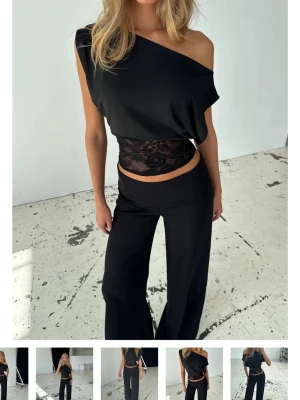 Svart oneshoulder topp med spetsdetal - Helt oanvänd och har lappen kvar. Trendig svart oneshoulder topp med bred spetsdetalj i midjan. 