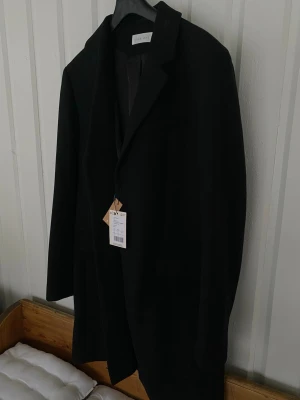 Svart kappa/rock herr storlek XL NY - Stilren svart kappa från Pier One med klassisk krage och knäppning framtill. Kappan har diskreta fickor som är osprättade, även en innerficka. Den är helt ny, säljes pga snabb viktnedgång. Djur och rökfritt hem 