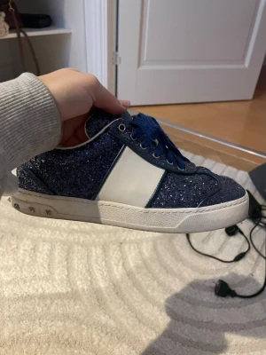 Valentino flycrew - Säljer ett par blå glittriga Valentino flycrew sneakers med vit sidopanel och blå snörning. Skorna har en låg profil och vita detaljer runt sulan samt små nitar på hälen. Alla nitar sitter kvar. Storlek 35 men passar 36-37.