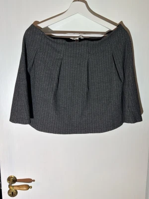 Grå kjol från H&M med ränder - Säljer en grå kjol med tunna vita ränder. Kjolen har en modern look. Perfekt att styla med en tröja med hög hals.