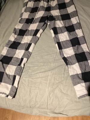 Rutiga pyjamasbyxor i svart och vitt - Mysiga pyjamasbyxor med stort rutmönster i svart och vitt. Byxorna har resår i midjan och dragsko för extra komfort. Perfekta för slappa dagar hemma eller när du vill ha det extra bekvämt på natten.