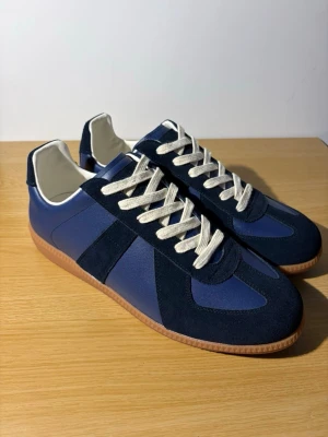 Maison margielas - Säljer ett par stilrena marinblå sneakers med kontrasterande vita snören och gummisula. Skorna har en mix av mocka och skinn, samt klassisk rund tå och platt sula. Perfekta för dig som gillar en clean och tidlös look.