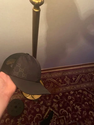 Gucci keps nylon svart  - Snygg svart keps från Gucci med klassiskt GG-mönster framtill och mesh på sidorna för extra ventilation. Justerbar snapback baktill med Gucci-logga. Perfekt accessoar för en trendig och avslappnad stil.