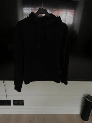 Svart hoodie från Jack & Jones - En stilren svart hoodie från Jack & Jones med klassisk huva och dragsnören. Hoodien har en känguruficka framtill och är tillverkad i mjukt material som känns skönt mot huden. Perfekt för en avslappnad look.