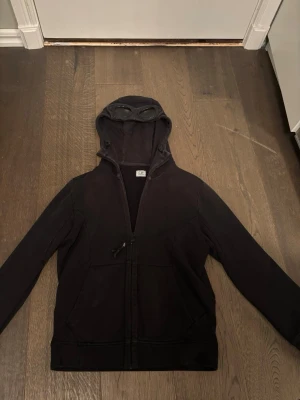 C.P. Company Hoodie - En väldigt väl använd hoodie med zip från cp company! Smått använd och väldigt långt material. Kontakta mig för intresse/frågor. ÄKTA 