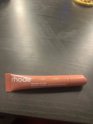 rhode Peptide Lip Tint Toast - Säljer ett rhode Peptide Lip Tint i färgen Toast. Läppbalsamet kommer i en smidig tub med skruvkork och har en snygg brunrosa nyans. Perfekt för att ge läpparna både fukt och en hint av färg. Materialet är plast och tuben är lätt att ta med i väskan.