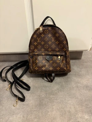 Liten, mönstrad ryggsäck. - Säljer en liten, mönstrad ryggsäck. Väskan har svarta justerbara axelremmar, guldfärgade dragkedjor och en praktisk ytterficka framtill.  Aldrig använd 