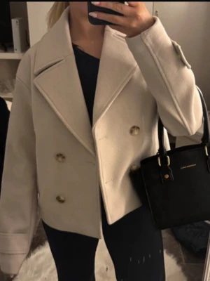 Beige kappa med guldknappar - En kappa ifrån Kappahl i storlek XS, ny köpt och använt ca 2-3 gånger. Extra knappar är även med som jag än inte hunnit ta av efter jag köpte den, men den får ni självklart med! Den är tjock varm och mysig. Nypris 900kr