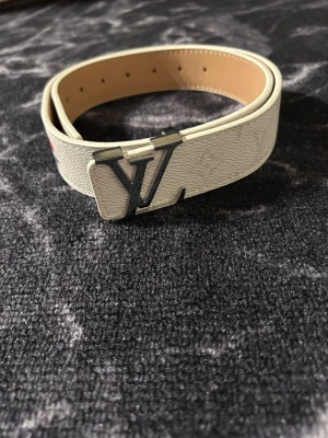 Vitt bälte med guldlogga - Stilrent vitt bälte med elegant guldlogga som ger en lyxig och modern känsla. Detta är inte ett original, utan ett högkvalitativt alternativ med noggrant utförda detaljer och snygg finish. Perfekt för dig som vill sticka ut och ge din outfit ett exklusivt lyft utan att betala premiumpris. Passar lika bra till vardag som till fest och kompletterar både ljusa och mörka outfits.Pris ej hugget i sten . Längd 105 cm.