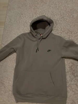 Beige Nike Air hoodie med huva - Säljer en beige Nike Air hoodie med huva och dragsnören. Hoodien har en klassisk känguruficka framtill och Nike Air-logga tryckt på bröstet. Tillverkad i mjukt bomullsmaterial som är perfekt för chill dagar. Snygg och enkel design som passar till det mesta.