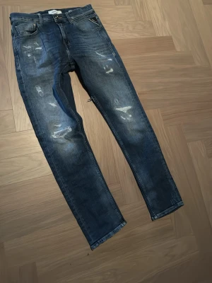 Blå slitna straight jeans - Säljer ett par blå jeans med slitningar och raka ben. Jeansen har klassisk femficksdesign och normal passform. Perfekta för dig som gillar en avslappnad och trendig stil. Aldrig använda, pris kan diskuteras 