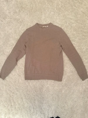 Beige stickad tröja med rund hals - En enkel och stilren beige stickad tröja med rund halsringning och ribbade muddar vid ärmslut och nederkant. Perfekt basplagg för lager på lager och passar till det mesta. Tröjan har en rak passform och är mjuk och bekväm.