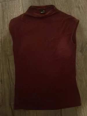Vinröd polotopp från Gina Tricot - Säljer en vinröd polotopp från Gina Tricot i storlek XXS. Toppen är ärmlös med hög krage och har en tight passform. Perfekt att styla med jeans eller kjol för en clean och trendig look.                                                                                 Tvättas innan köp, såg nu att den fick en fläck på bilden  men finns ingen fläck i verkligheten.           Priset kan diskuteras 