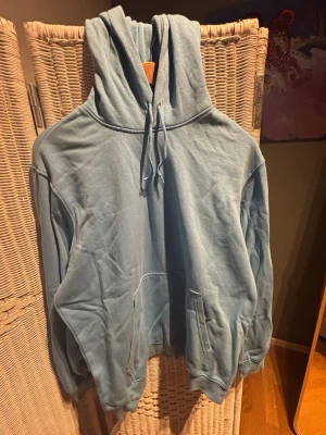 Ljusblå hoodie från Weekday - Säljer en ljusblå hoodie från Weekday med stor huva och dragsko. Hoodien har en klassisk känguruficka framtill och ribbade muddar vid ärmslut och nederkant. Tillverkad i mjuk bomullsblandning som är skön att ha på sig.