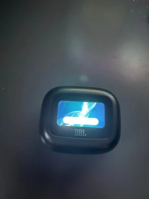 JBL bärbar trådlösa hörlurar med display - Snygg och kompakt bärbara hörlurar från JBL med inbyggd färgdisplay. Svart, rundad design i plast som visar låtinfo och batteristatus direkt på skärmen. Perfekt för att ta med sig överallt och styra musiken smidigt.