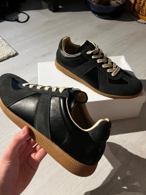 Svarta sneakers med beige sula - Stilrena svarta sneakers med beige snörning och kontrasterande gummisula. Skorna har en klassisk rund tå och är tillverkade i en mix av skinn och mocka. Perfekta för dig som gillar en clean och tidlös look.