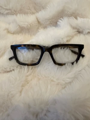 Gucci fyrkantiga solglasögon brun - Snygga glasögon från Gucci med markerad fyrkantig båge i brunmelerad plast. Diskret Gucci-logga på skalmen. Perfekt accessoar för dig som vill sticka ut med en trendig och exklusiv look. Använda 3 gånger. Köpta för 4000kr Dem är äkta! 