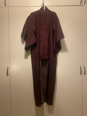 Vinröd kimono i bomull - Säljer en vinröd kimono med breda ärmar och tillhörande skärp. Kimonon är gjord i ett tunt tyg, gissningsvis silke. Vackert vågmönster. Köp i Japan. Oanvänd. 