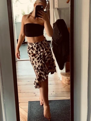 Leopardmönstrad omlottkjol med volang - Säljer en snygg leopardmönstrad omlottkjol med volangkant. Kjolen har en beige bas med svarta och bruna fläckar och är i en luftig, flowy modell som slutar strax under knät. Perfekt för dig som vill sticka ut lite extra!